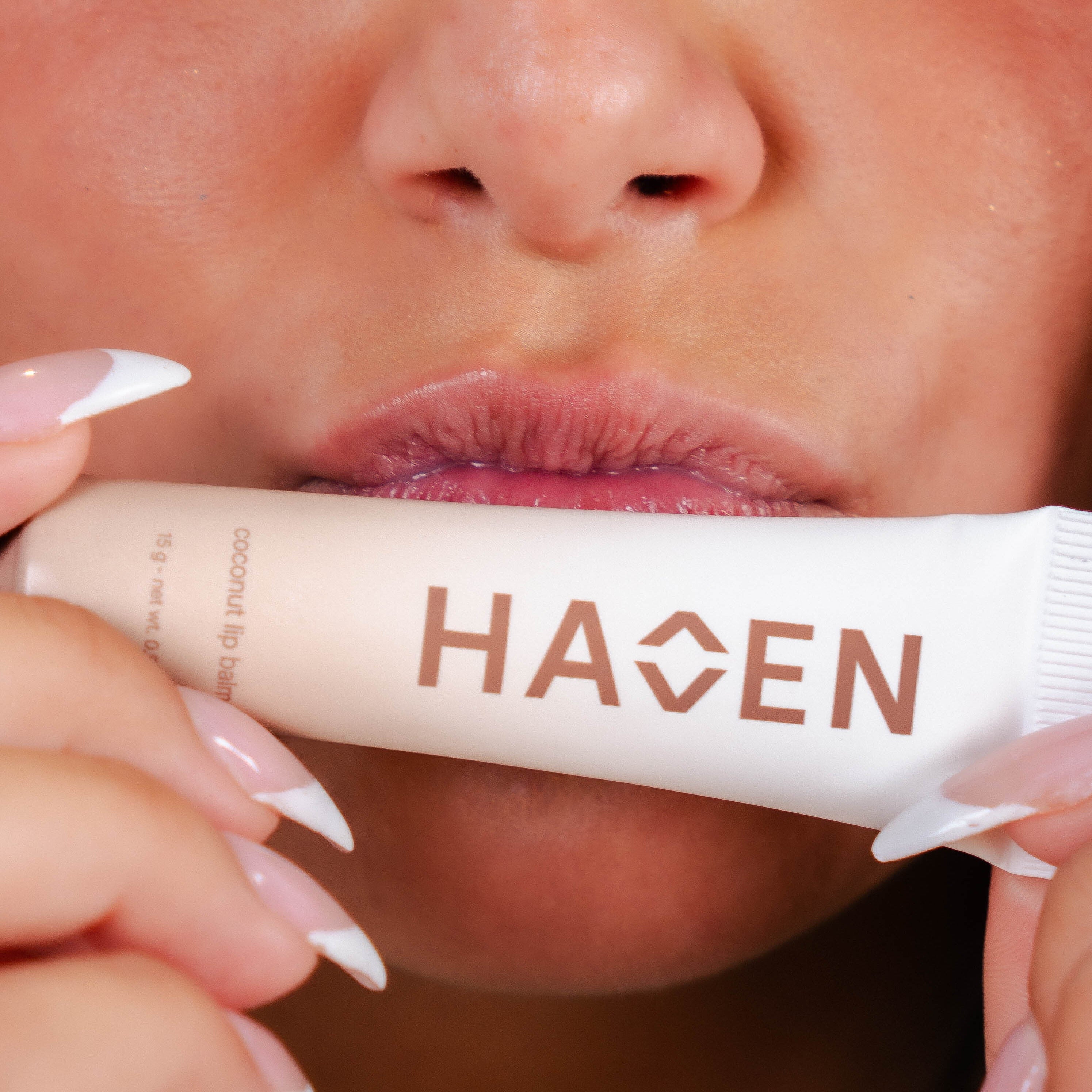 A woman holding coconut lip balm up to her lips.