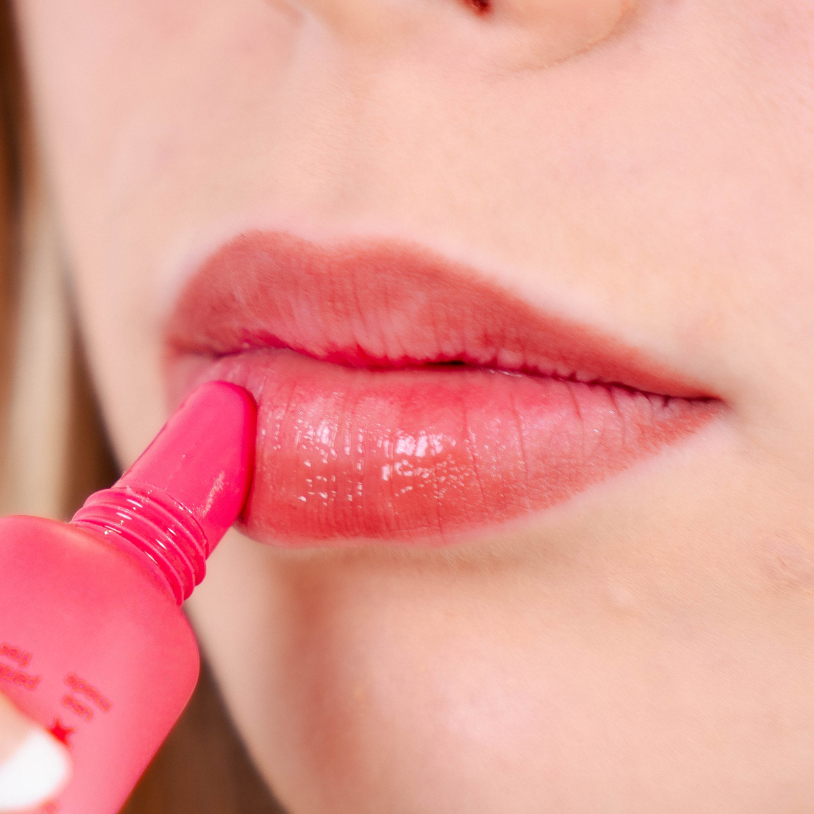 Close-up of a woman applying sugar rose lip balm to her lips.