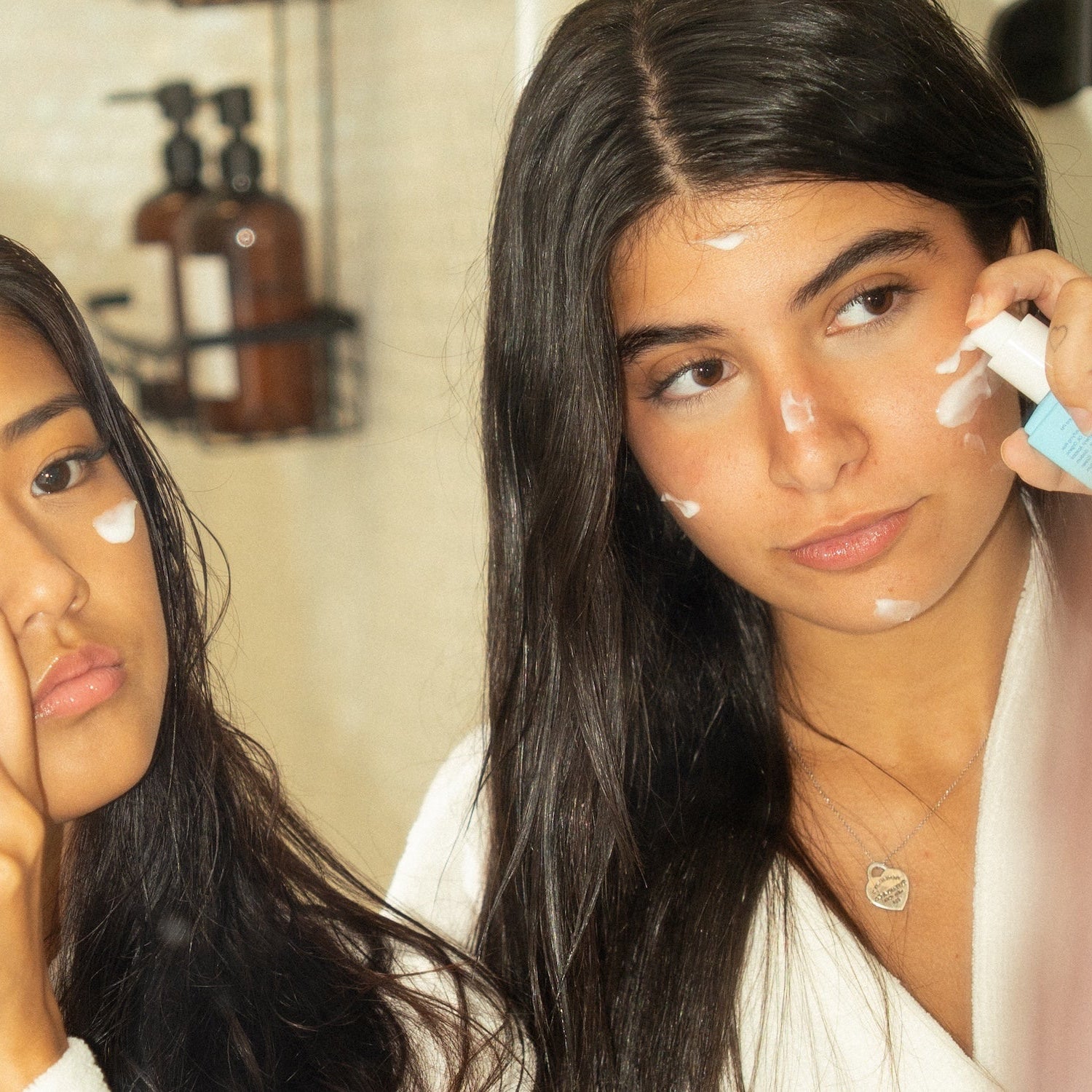 Two women applying Haven moisturizer to their faces in a bathroom setting.
